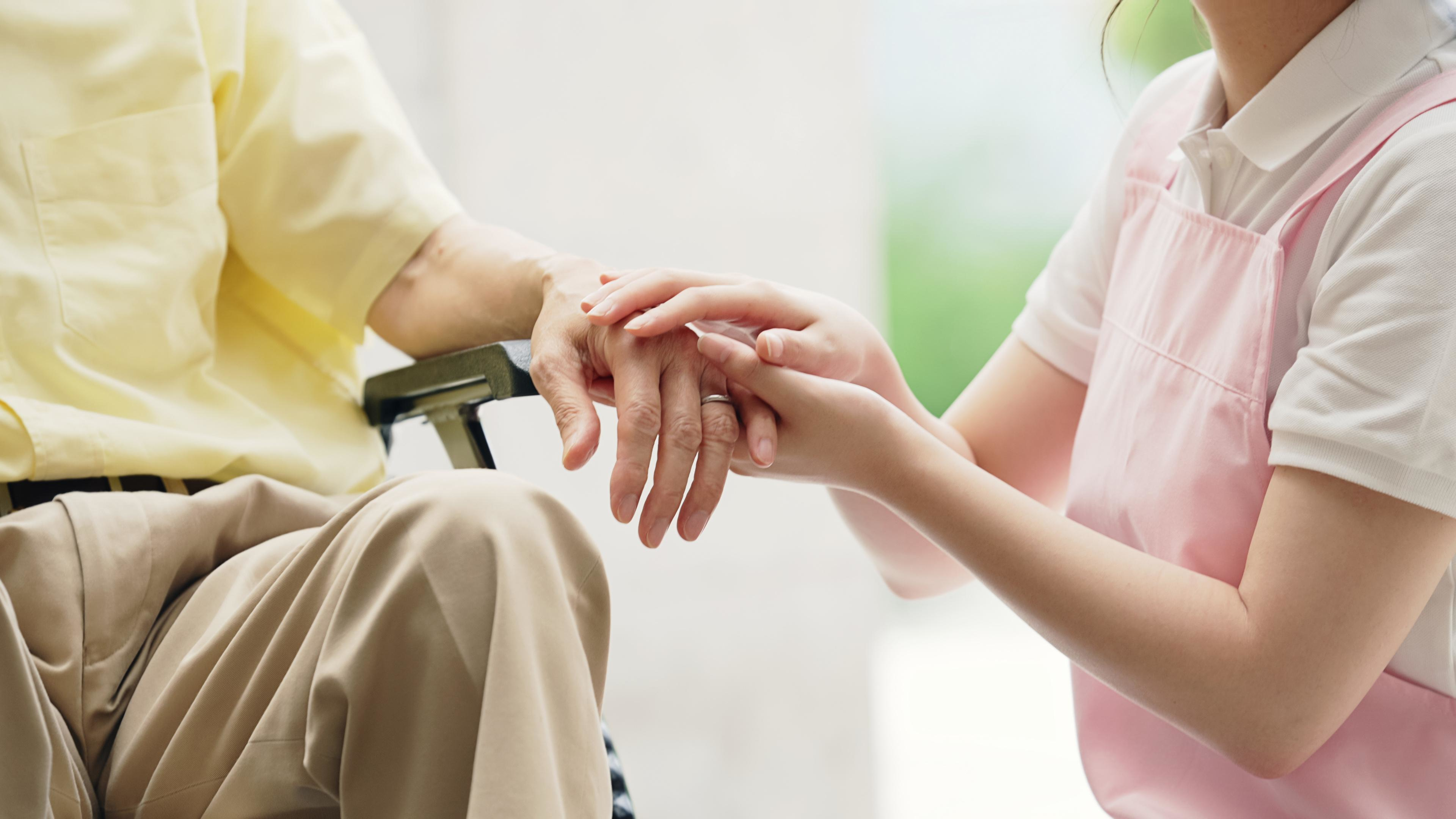 介護士が高齢者の手を優しく握っている様子